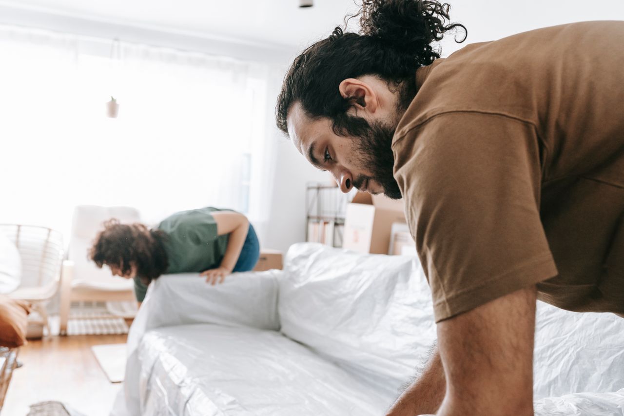 A couple wrapping furniture in a bright apartment, preparing to move.