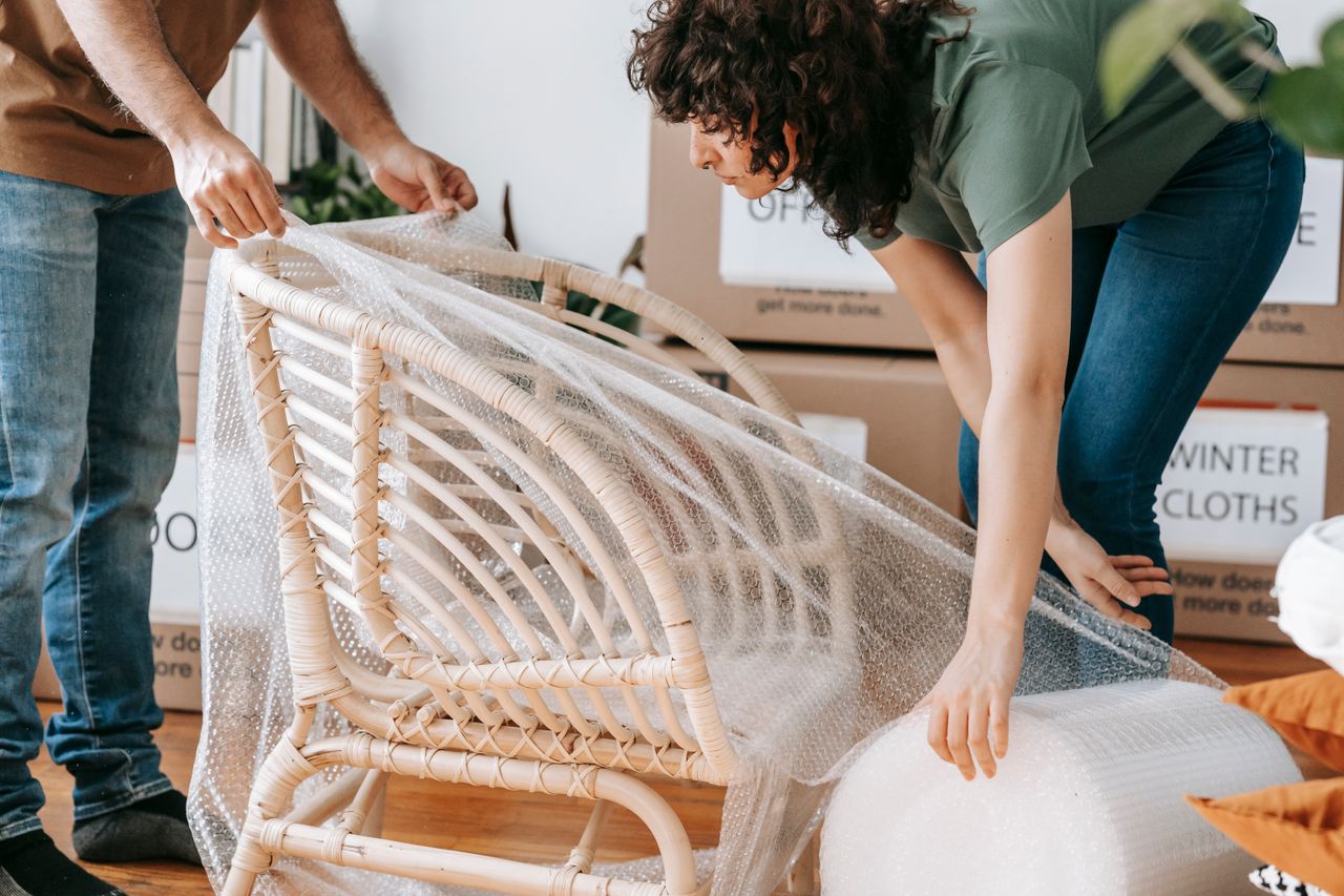 hero-img A couple uses bubble wrap to protect a chair while packing up their home for relocation.
